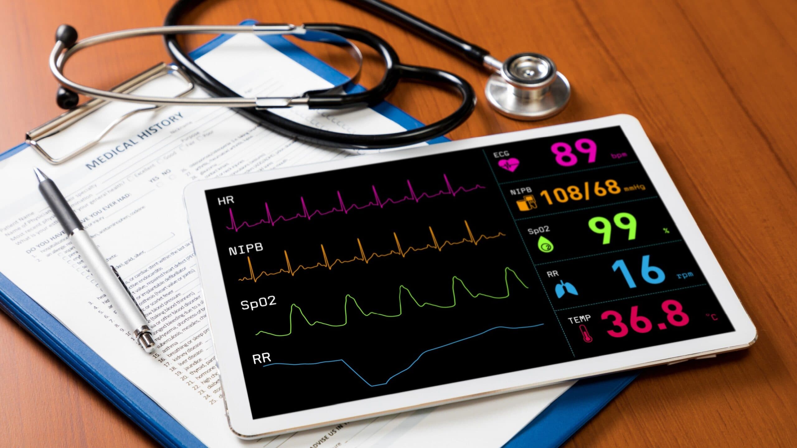 Image of an tablet with patient vital signs on, with a clipboard, pen and stethoscope