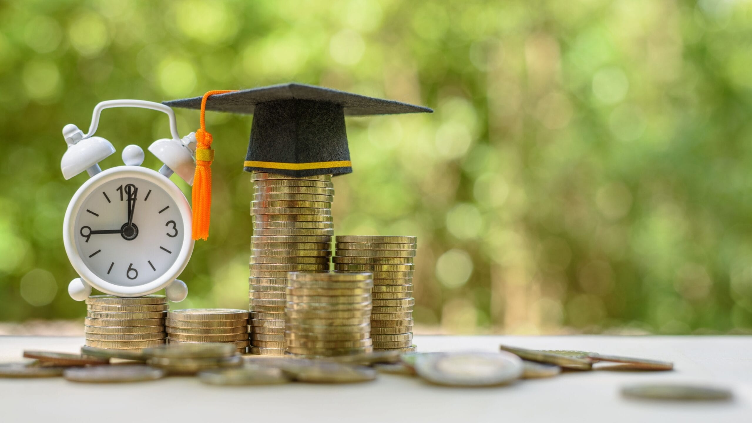 Image of stacks of coins with a clock on one and a graduation cap on another against a green background
