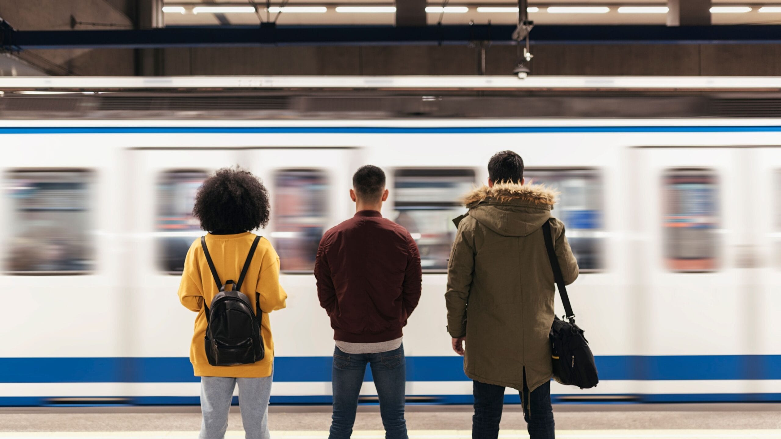 Image of three students stood with their backs to the camera on a train platform as a train passes