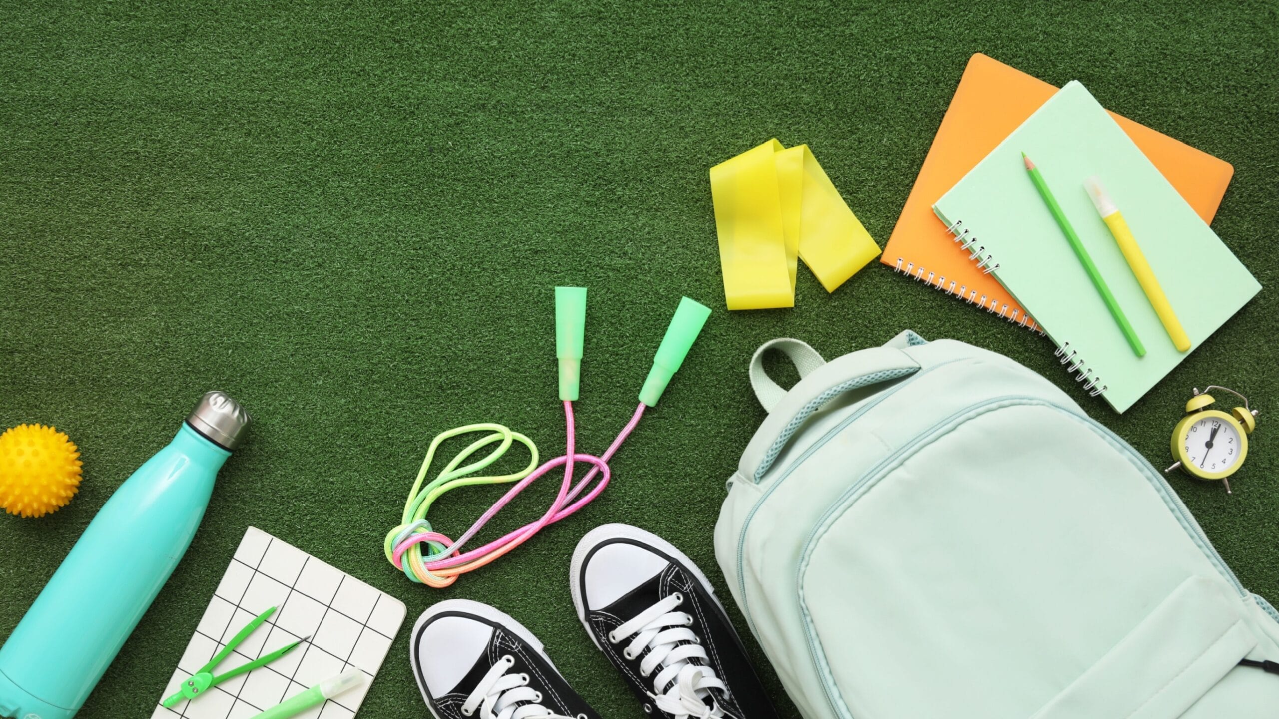Image of green grass with a backpack, notebook, pens, skipping rope and water bottle.