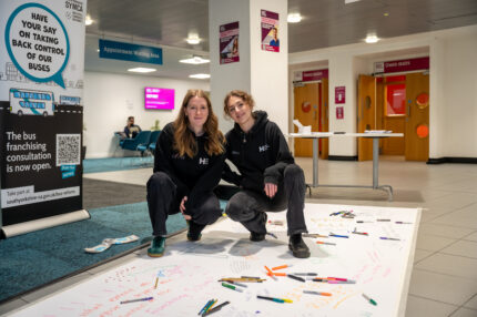 Two student officers stood on a long piece of paper with feedback from commuter students on