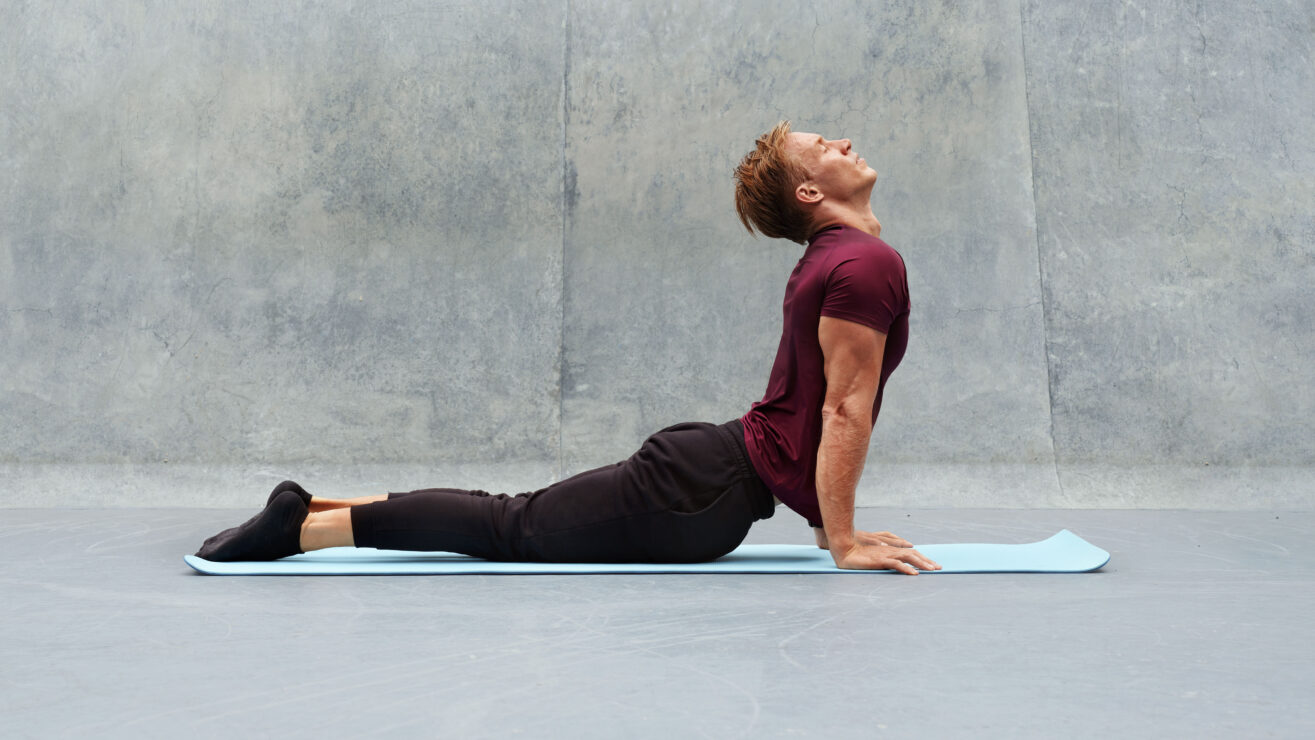 Young,Man,Stretching,On,Yoga,Mat,Against,Concrete,Wall,Outdoors.