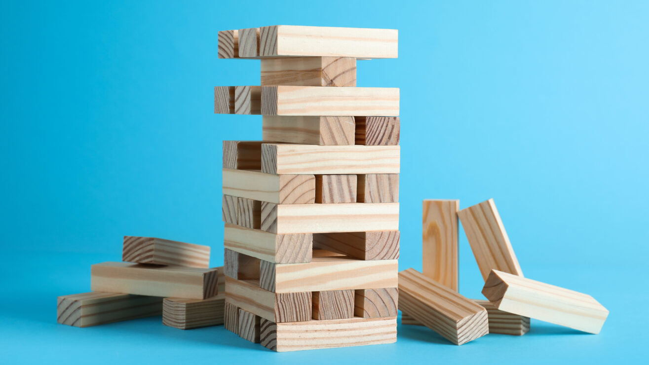 Jenga,Tower,Made,Of,Wooden,Blocks,On,Light,Blue,Background