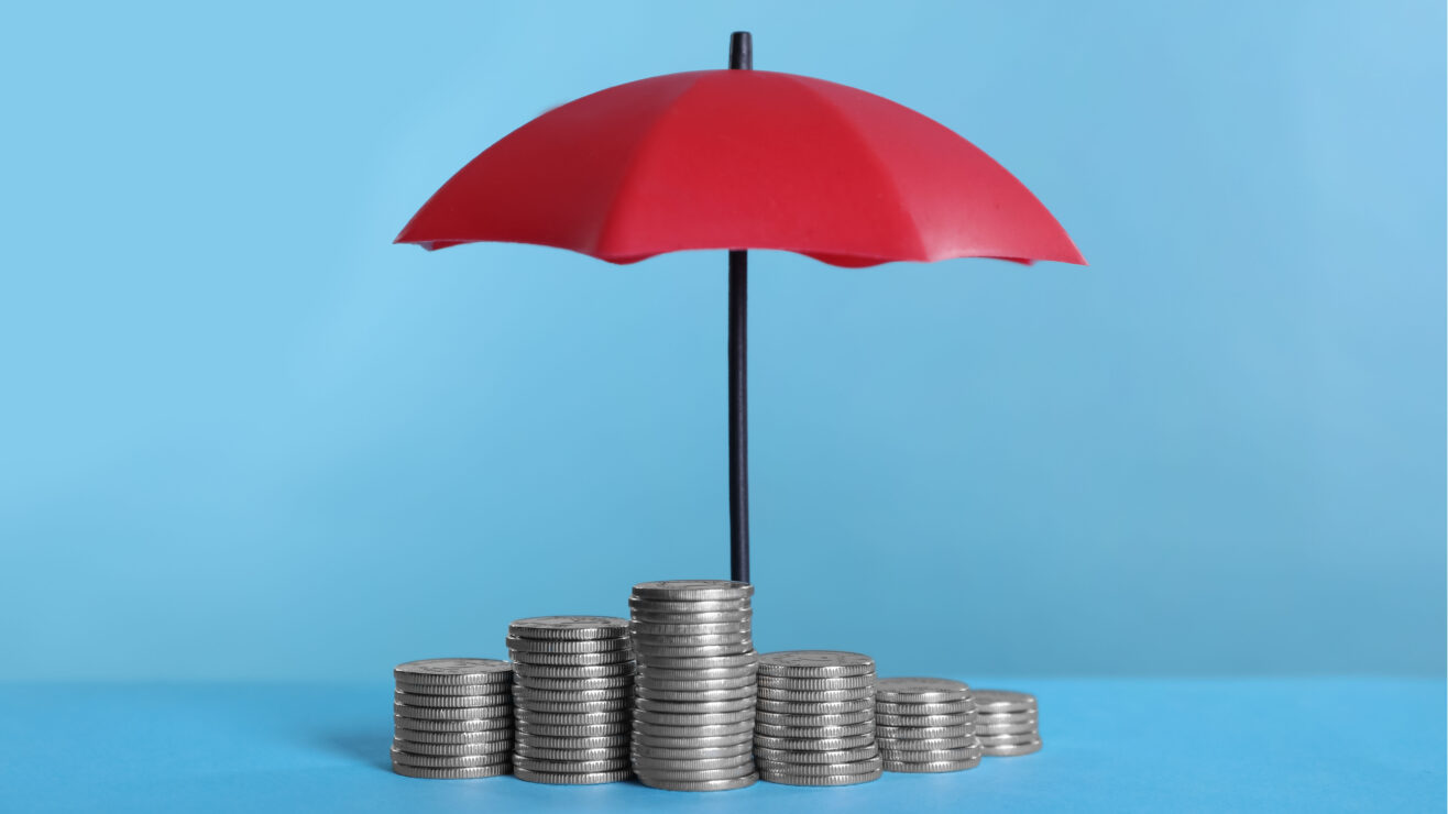 Small,Umbrella,And,Coins,On,Light,Blue,Background