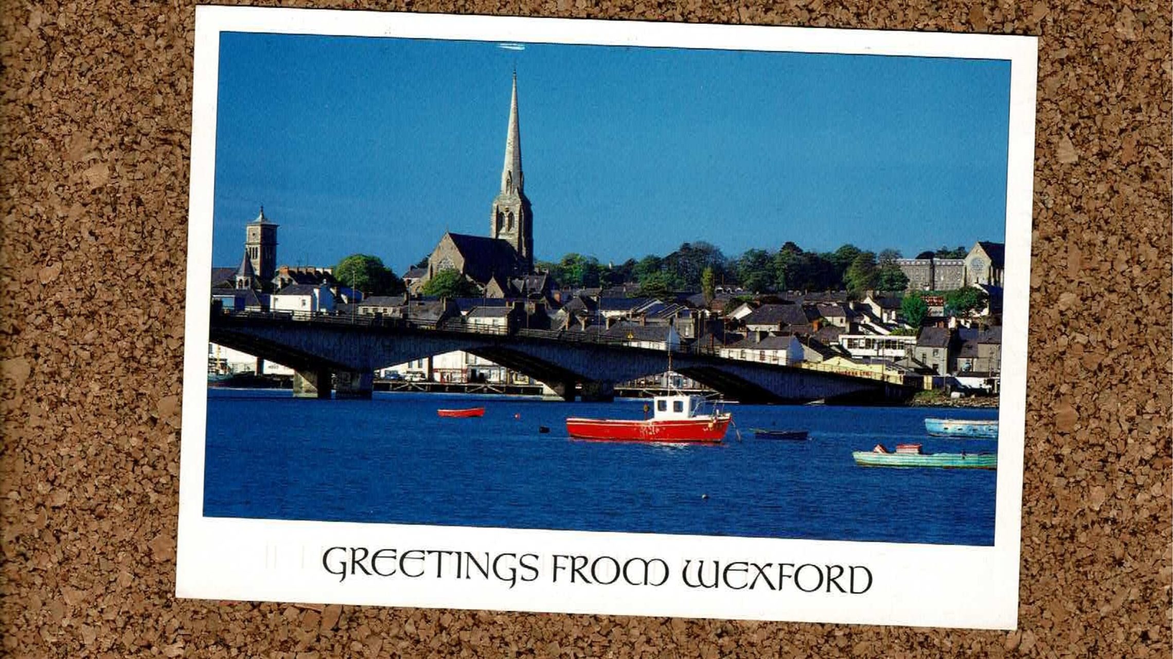 Image of a corkboard with a postcard on of SETU in Ireland with the text "greetings from Wexford"