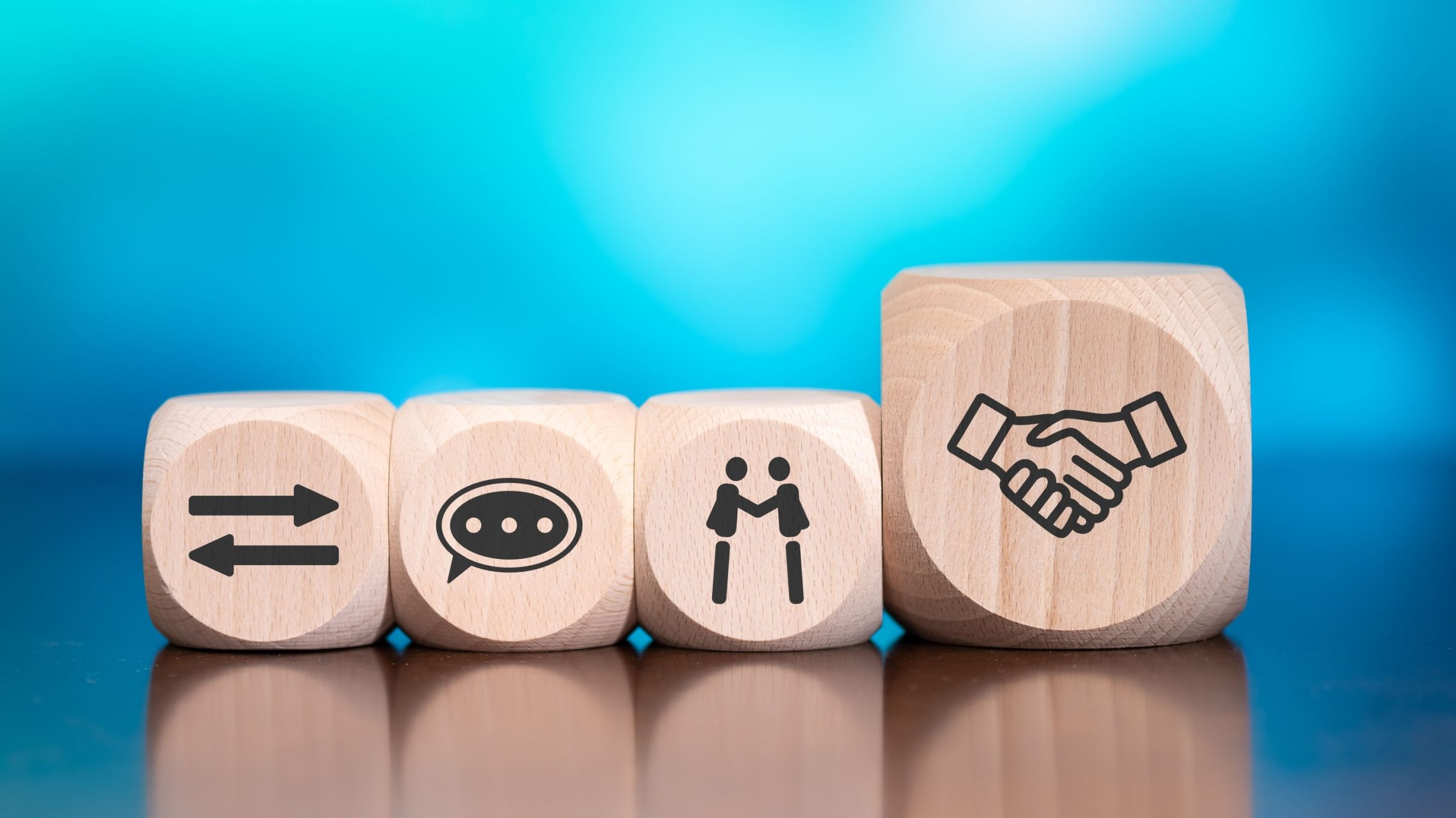 Blue background with four wooden blogs with four symbols on: two arrows, a speech bubble, two people shaking hands and a shaking hands icon